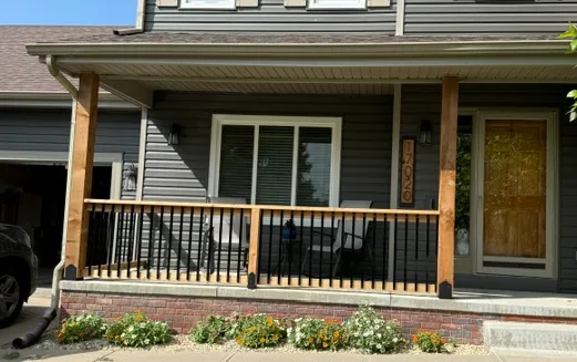 Covered front porch with cedar posts and black metal railing on a gray two story home