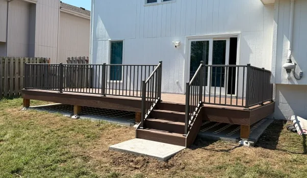 Composite deck in dark brown with black metal railing and steps down to a concrete pad